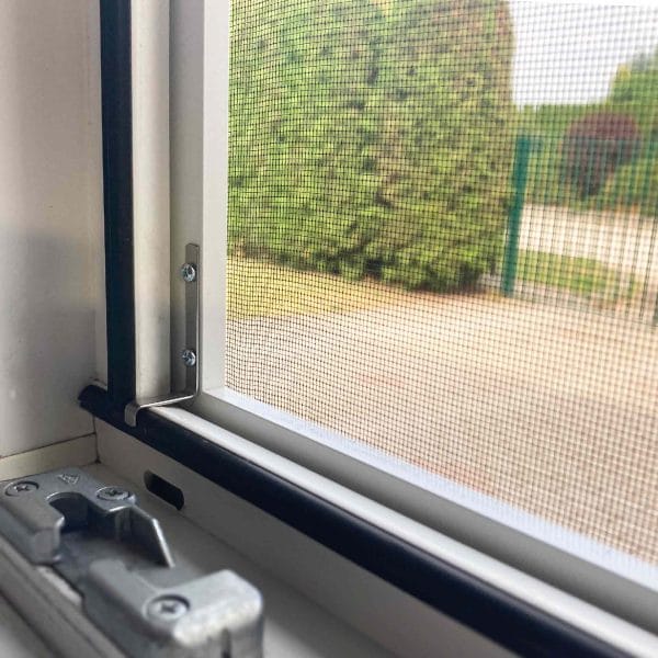 Insect_net_frame_03 Close-up of Fliegengitter Fenster - mit Rahmen with latch, showing greenery and a gravel path outside.